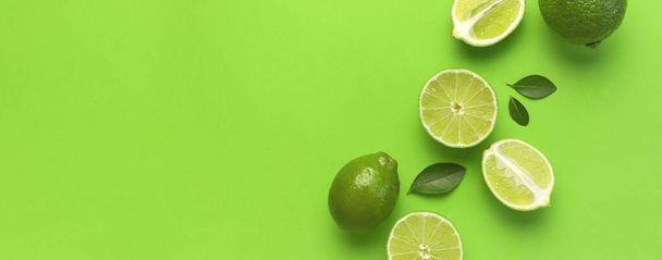 Fresh juicy lime and green leaves on bright green background. Top view flat lay copy space. Creative food background, tropical fruit, vitamin C, citrus. Composition with whole and slices of lime - Foto, imagen