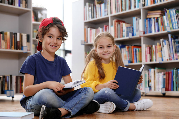 Милі маленькі діти читають книги на підлозі в бібліотеці
 - Фото, зображення