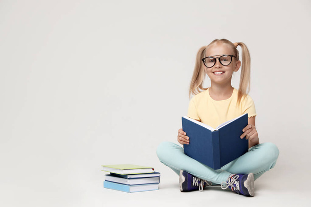 Cute little girl with glasses reading book on grey background. Space for text - Foto, immagini