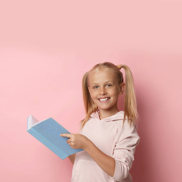 Portrait of cute little girl reading book on pink background - Photo, image