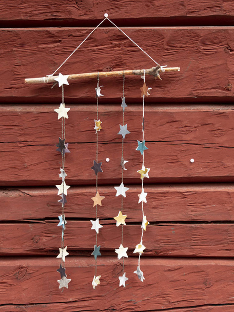 Handgemaakte decoratie van zilveren papieren sterren hangend aan een stok tegen de rode muur - Foto, afbeelding