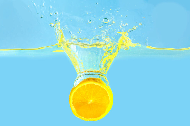 Πτώση πορτοκαλί κομματιού σε νερό με φόντο το φως - Φωτογραφία, εικόνα