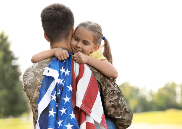 Father in military uniform with American flag and his daughter at sunny park - Фото, изображение