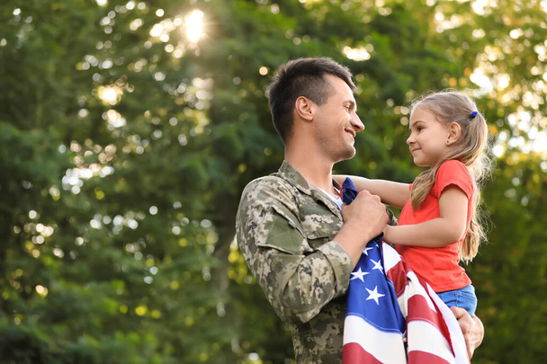 Father in military uniform with American flag holding his little daughter at green park - Zdjęcie, obraz