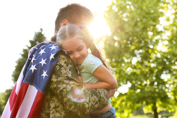 Father in military uniform with American flag holding his little daughter at green park - Foto, Imagen
