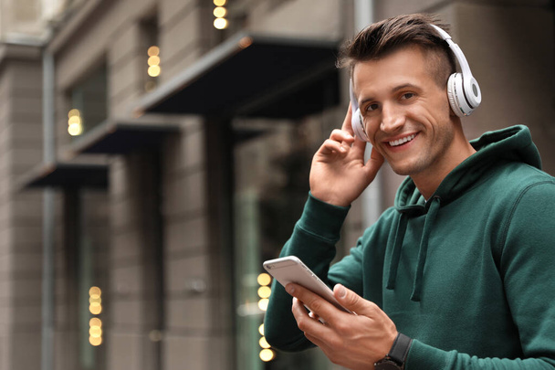 Portrait of handsome man with headphones and smartphone listening to music on city street. Space for text - Foto, Bild