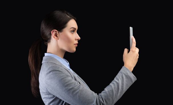 Бизнесвумен с помощью смартфона и распознавания лиц стоять, черный фон
 - Фото, изображение