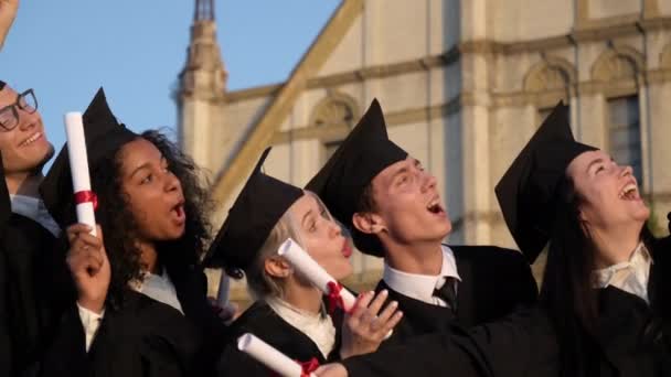Mieszane wyścigi absolwentów znajomych w czarne tradycyjne suknie i czapki podejmowania selfie na smartfonie. - Materiał filmowy, wideo