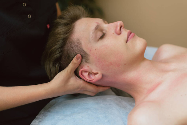 O massagista faz uma massagem facial a um jovem. Um homem é massageado em uma mesa de massagem
 - Foto, Imagem