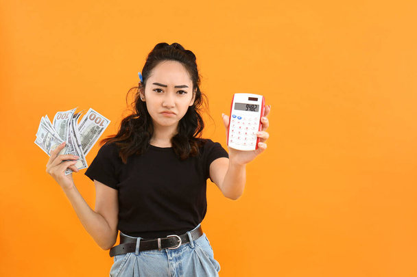 Szomorú ázsiai nő pénzzel és számológép színes háttér - Fotó, kép