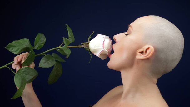 beautiful bald woman in a black leather corset holds a pink rose in her hands and kisses a flower. adventures of strange people. - Photo, Image