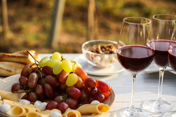 Red wine and snacks served for picnic on white wooden table outdoors - Foto, afbeelding