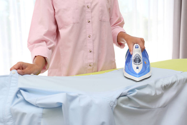 Young woman ironing clean shirt at home, closeup. Laundry day - Foto, Bild