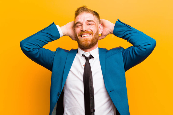 young red head businessman looking happy, carefree, friendly and relaxed enjoying life and success, with a positive attitude against orange background - Фото, изображение
