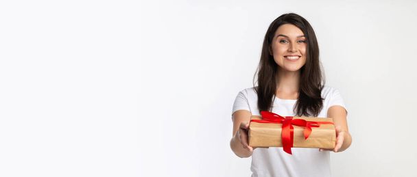 Cheerful Woman Giving Wrapped Gift Box Standing, White Background, Panorama - Foto, imagen