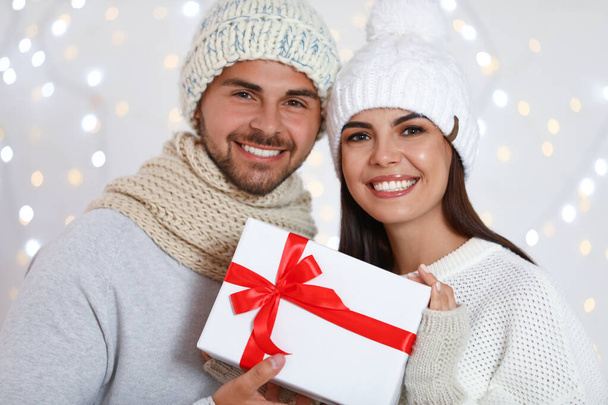 Lovely young couple with gift box against blurred festive lights. Christmas celebration - Foto, imagen