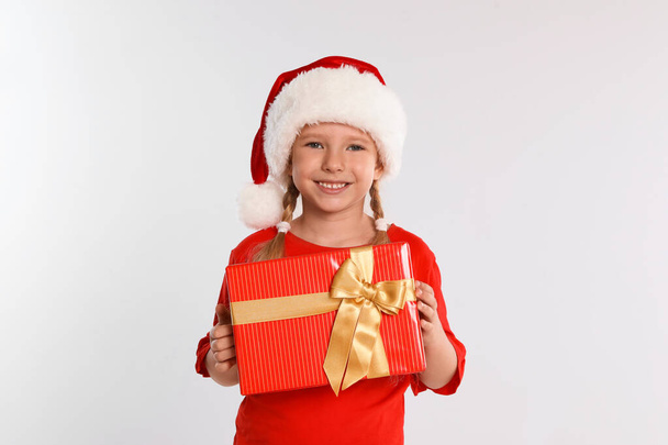 Щаслива маленька дитина в Санта-Каті з подарунковою коробкою на світло-сірому фоні. Свято Різдва - Фото, зображення