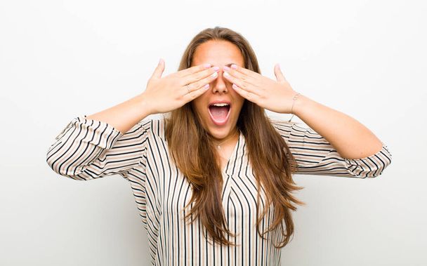 young woman smiling and feeling happy, covering eyes with both hands and waiting for unbelievable surprise against white background - Foto, immagini