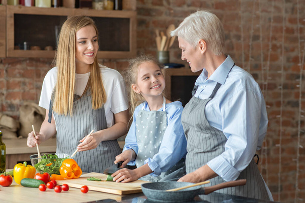 Volwassen vrolijke dames leren kleine meisje hoe om te koken - Foto, afbeelding