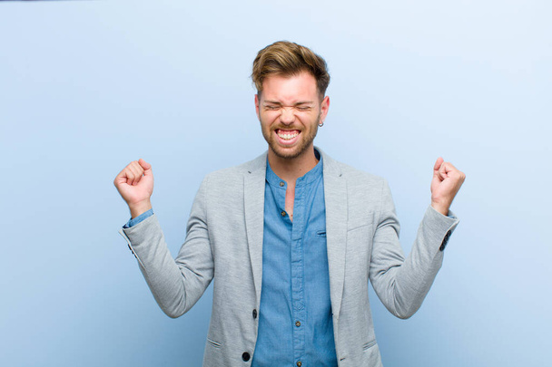 young businessman looking extremely happy and surprised, celebrating success, shouting and jumping against blue background - Foto, immagini