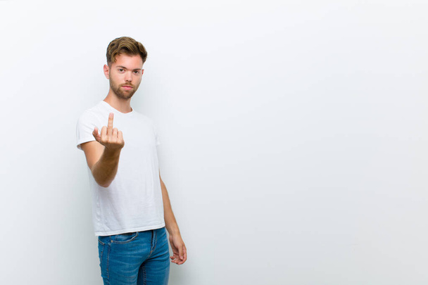 young man feeling angry, annoyed, rebellious and aggressive, flipping the middle finger, fighting back against white background - 写真・画像