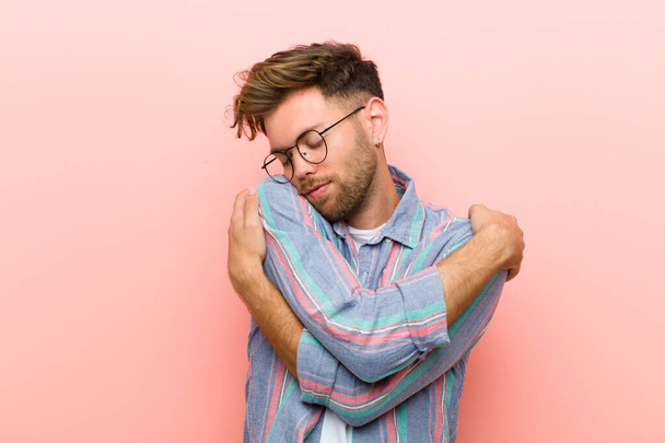 young man feeling in love, smiling, cuddling and hugging self, staying single, being selfish and egocentric against pink background - Fotoğraf, Görsel