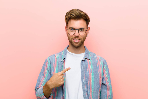 young man looking proud, confident and happy, smiling and pointing to self or making number one sign against pink background - Foto, imagen