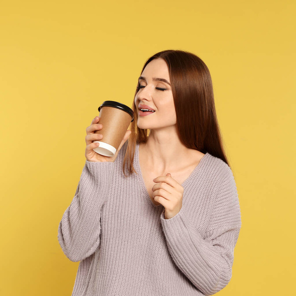 Beautiful young woman in sweater with drink on yellow background. Winter season - Valokuva, kuva