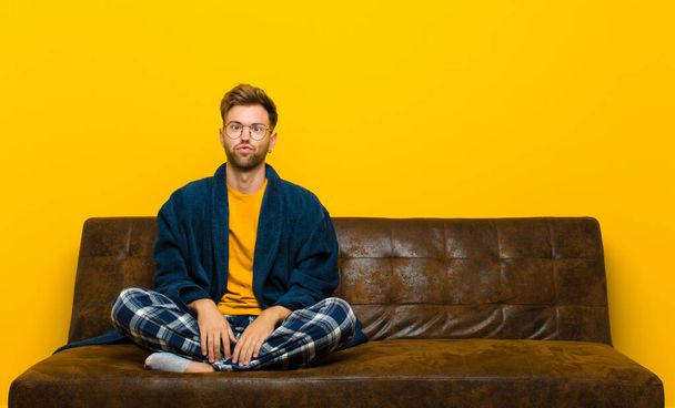 young man wearing pajamas looking goofy and funny with a silly cross-eyed expression, joking and fooling around . sitting on a sofa - Photo, Image
