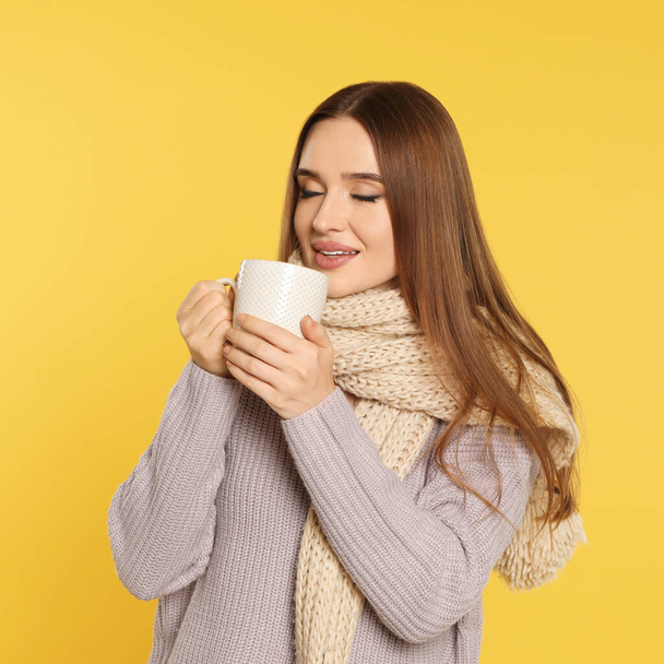 Beautiful young woman in sweater with drink on yellow background. Winter season - Фото, зображення