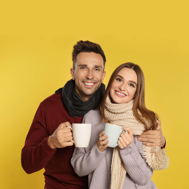 Šťastný mladý pár v teplém oblečení s poháry na žlutém pozadí. Zimní sezóna - Fotografie, Obrázek