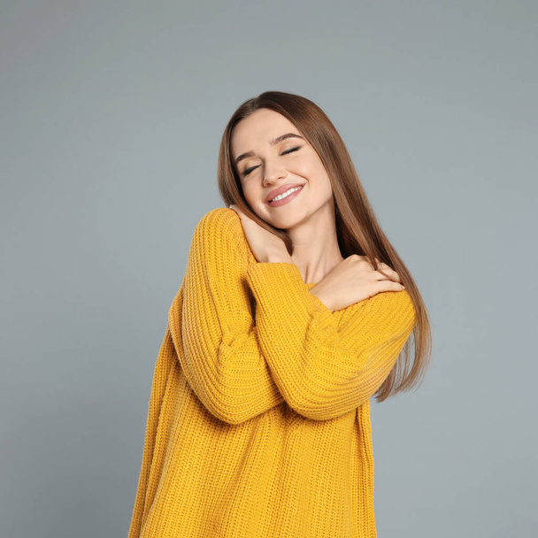 Beautiful young woman in yellow sweater on grey background. Winter season - Фото, зображення