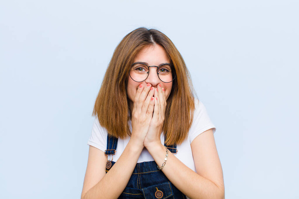young pretty woman happy and excited, surprised and amazed covering mouth with hands, giggling with a cute expression against blue background - Foto, Bild
