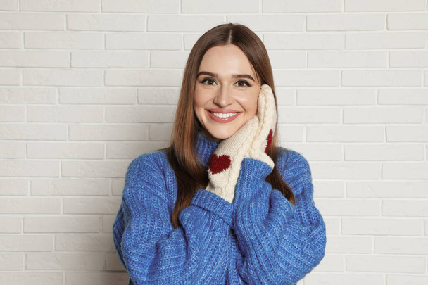 Beautiful young woman in mittens and blue sweater near white brick wall. Winter season - Fotoğraf, Görsel