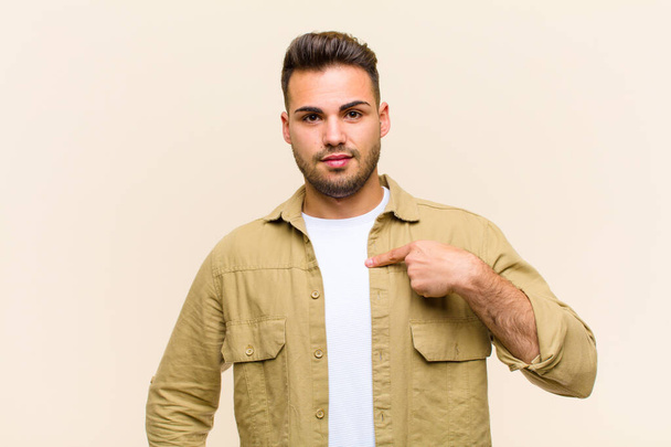 young hispanic man looking happy, proud and surprised, cheerfully pointing to self, feeling confident and lofty against isolated background - Fotografie, Obrázek