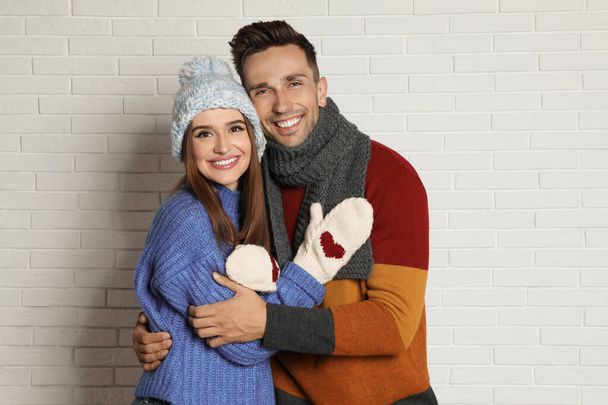 Happy young couple in warm clothes near white brick wall. Winter season - Foto, Imagem
