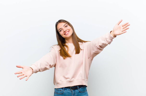 young pretty woman smiling cheerfully giving a warm, friendly, loving welcome hug, feeling happy and adorable against white background - Foto, afbeelding