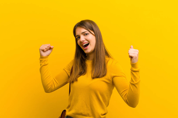 молода красива жінка, що кричить тріумфально, виглядає як схвильований, щасливий і здивований переможець, святкуючи на помаранчевому фоні
 - Фото, зображення