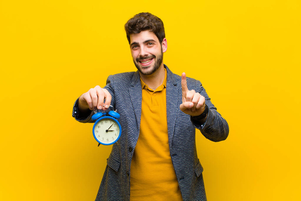 young handsome man with an alarm clock against orange background - Zdjęcie, obraz