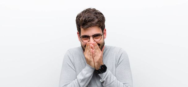 young manager man looking happy, cheerful, lucky and surprised covering mouth with both hands against white wall - Photo, image