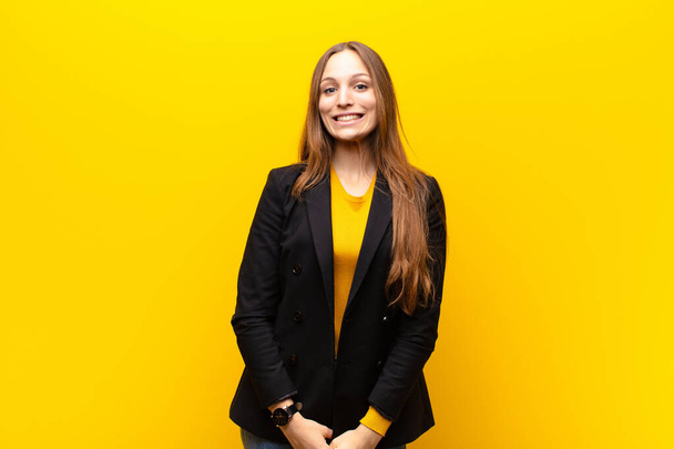 young pretty businesswoman looking happy and goofy with a broad, fun, loony smile and eyes wide open against orange background - Foto, Imagen