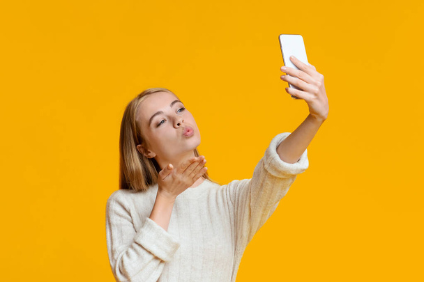 Kokettierendes Mädchen macht Selfie auf Smartphone und schickt Luftkuss - Foto, Bild