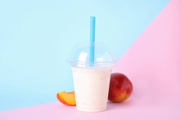 Tasty peach milk shake in plastic cup and fresh fruit on color background - Фото, зображення