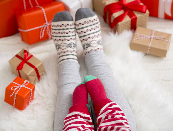 Πόδια του μωρού και της μαμάς σε χειμερινές κάλτσες, κάθεται στο πάτωμα με χριστουγεννιάτικα δώρα - Φωτογραφία, εικόνα