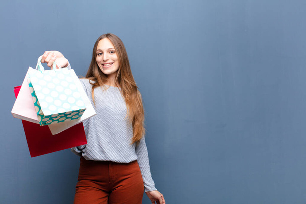 young pretty woman with shopping bags against blue wall with a copy space - Photo, Image