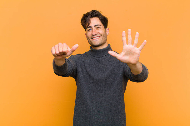 young handsome man smiling and looking friendly, showing number six or sixth with hand forward, counting down against orange background - 写真・画像
