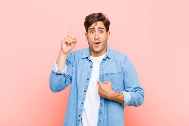 young handsome man feeling proud and surprised, pointing to self confidently, feeling like successful number one against pink background - Photo, Image