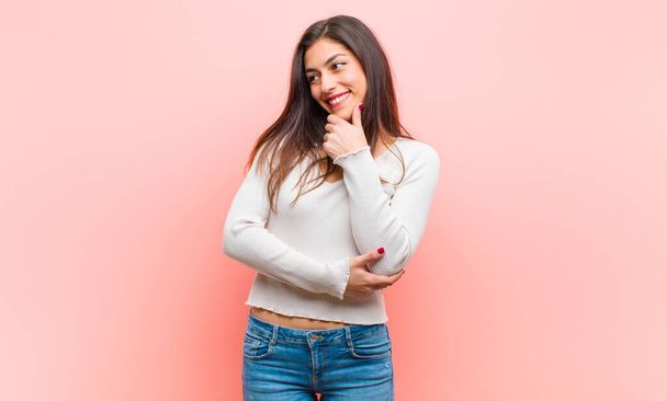 young  pretty woman smiling with a happy, confident expression with hand on chin, wondering and looking to the side against pink background. - Photo, Image