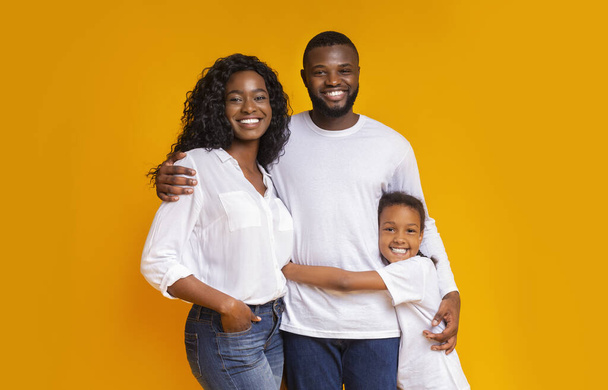 Hermosa familia afroamericana con hija abrazando sobre fondo amarillo
 - Foto, imagen