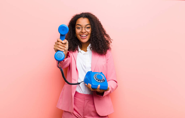 young black pretty woman with a vintage telephone against pink wall background - Fotografie, Obrázek